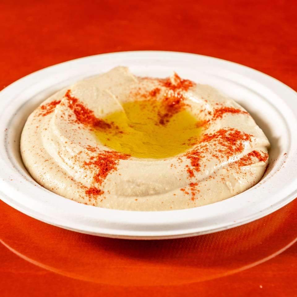 Creamy hummus with a pool of olive oil and a sprinkle of paprika, served in a white bowl.