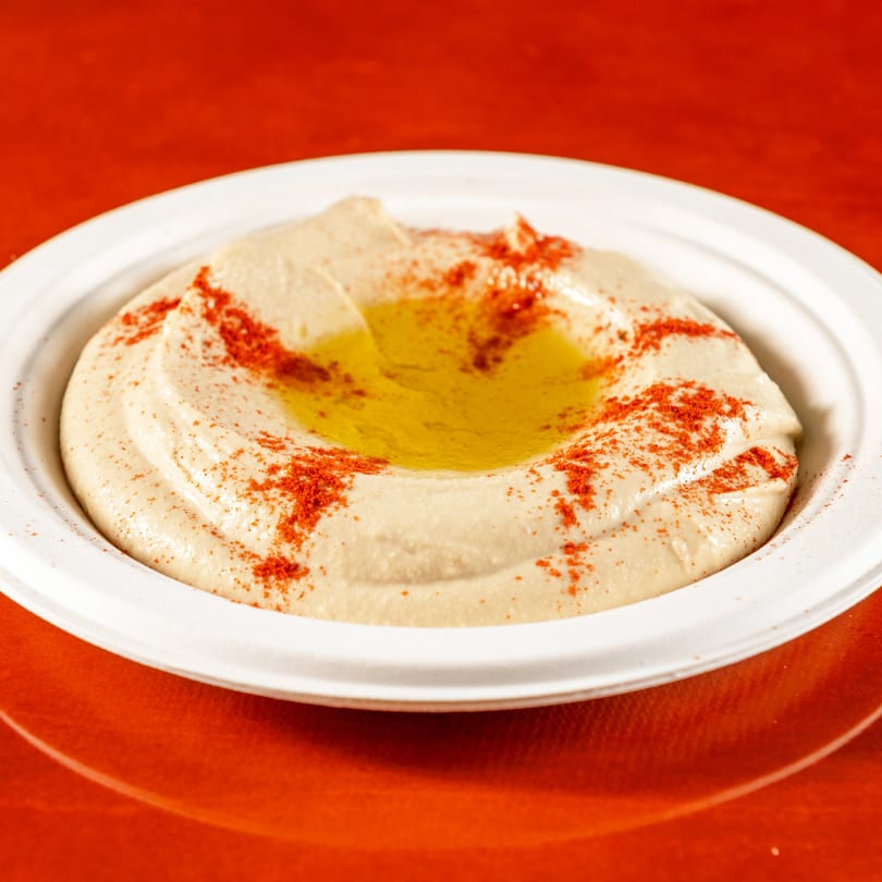 Creamy hummus with a pool of olive oil and a sprinkle of paprika, served in a white bowl.