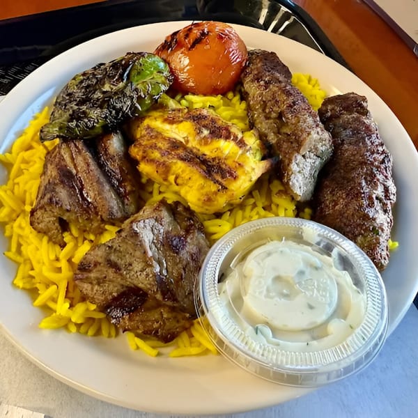 A Mediterranean platter with grilled meats, yellow rice, charred vegetables, and a side of sauce.