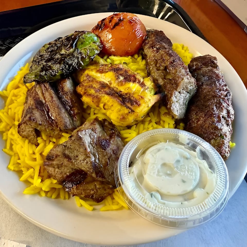 A Mediterranean platter with grilled meats, yellow rice, charred vegetables, and a side of sauce.