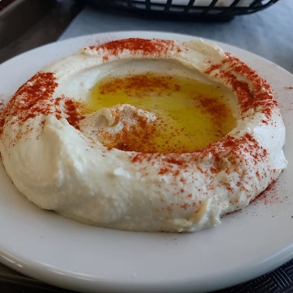 Creamy hummus with a pool of olive oil and a sprinkle of paprika on a white plate.
