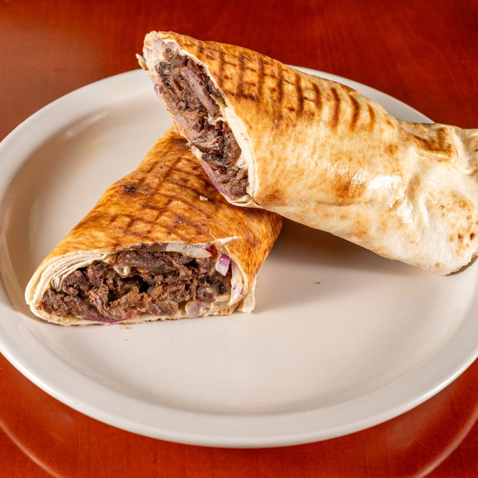 Two grilled Mediterranean shawarma wraps, filled with meat and onions, on a white plate.